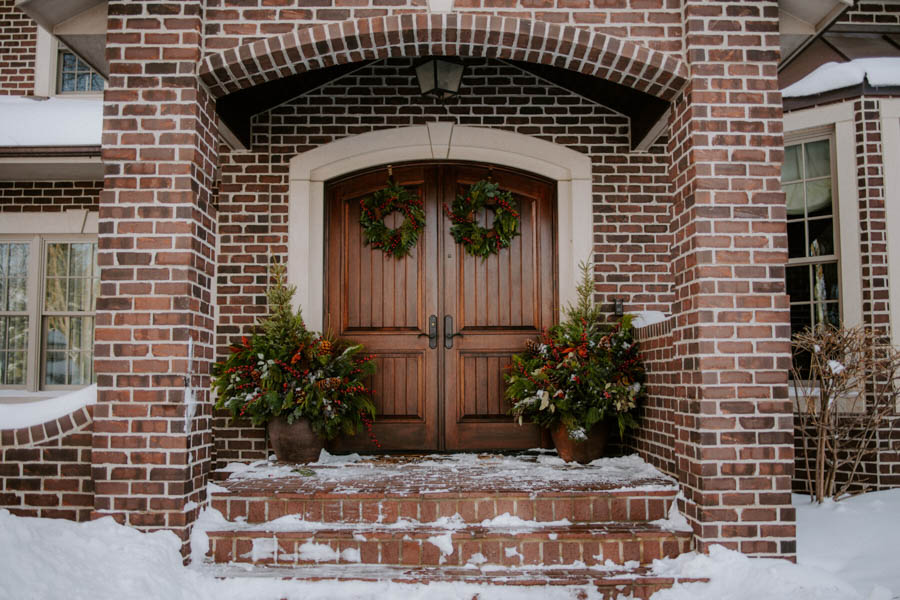 front door of a brick home with holiday planters and wreaths