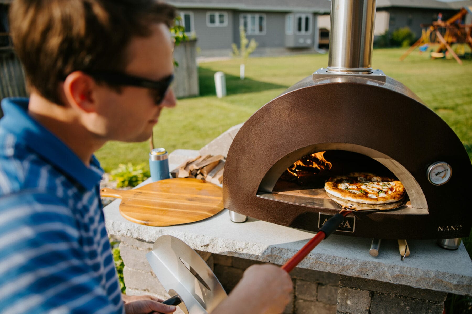 man removes pizza from his outdoor pizza oven