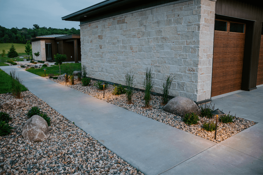 rock bed with plants and landscape lighting in front of a modern home
