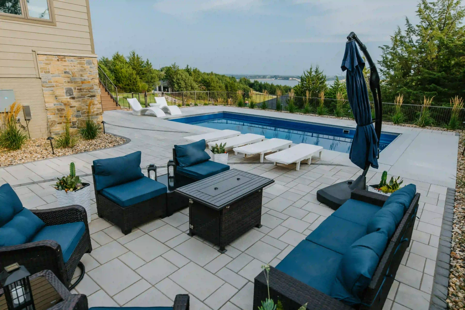 a blue and black outdoor furniture set is staged on a techo-bloc paver patio alongside a backyard pool overlooking the missouri river