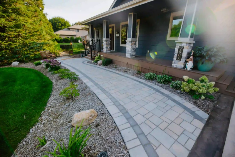 a paver patio walkway with mulch bed and plantings in front of a blue home